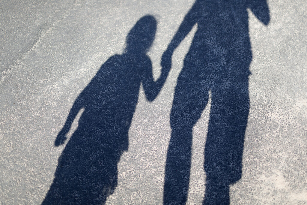 Siluett av ett barn och en vuxen som håller varandra i handen.